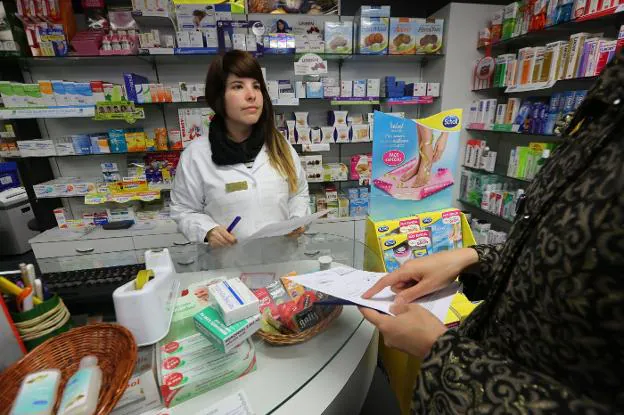 Una clienta solicita unos medicamentos en una farmacia avilesina. 