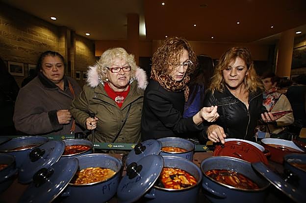 Un grupo de mujeres observa las potas de fabada presentadas al concurso. 