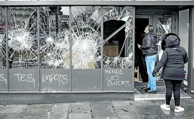 Dos personas observan los daños que presenta una cafetería de París tras las protestas del sábado.