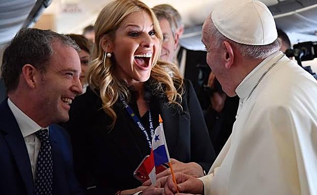 El papa Francisco (d) ondea una bandera panameña junto a los periodistas que viajan con él en el avión. 