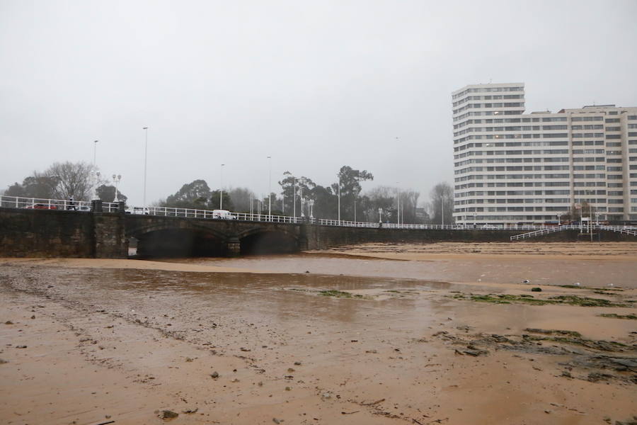 El paseo gijonés del Muro ha amanecido con algunas de sus escaleras cerradas debido a los daños causados por el temporal de lluvia y viento. Operarios de Emulsa han procedido a la limpieza de la arena depositada en el paseo tras la pleamar.