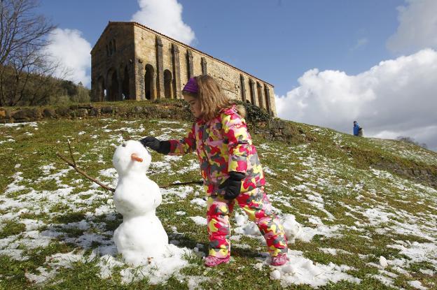 Una niña hace un muñeco de nieve, frente a Santa María del Naranco. 