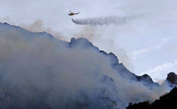 Imagen. Un helicóptero descarga sobre las laderas próximas al embalse de Calabazos donde se reavivó el fuego a media tarde.