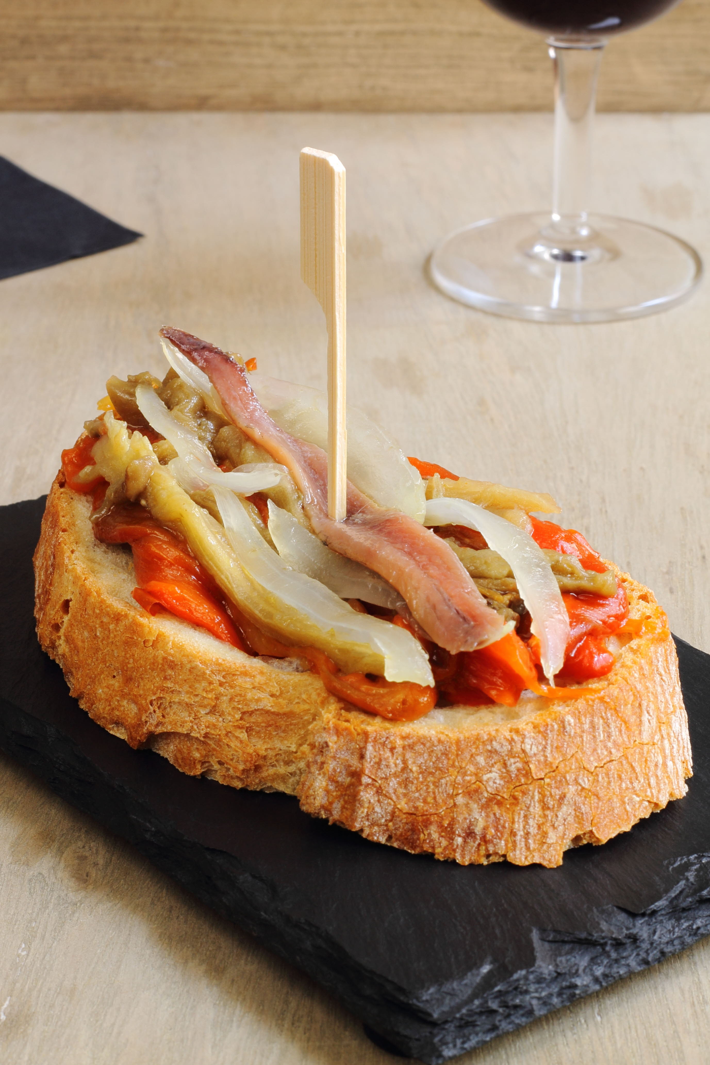 Tostada de pan con pimientos, cebolla y anchoa. 