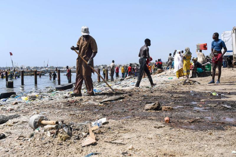 La gente camina cerca de llantas, desechos plásticos y peces muertos en la bahía de Hann en Dakar.