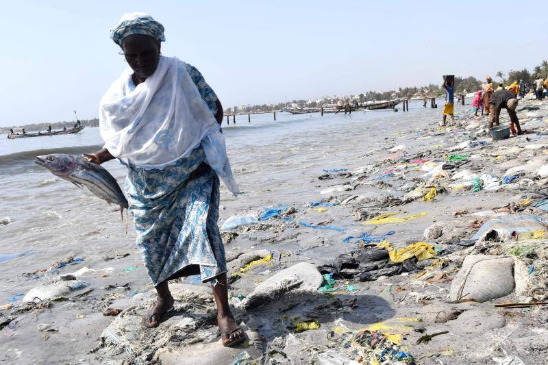 Una mujer que sostiene un pez camina sobre llantas y desechos plásticos en la altamente poblada bahía de Hann en Dakar