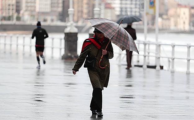 Una mujer camina bajo la lluvia en Gijón.
