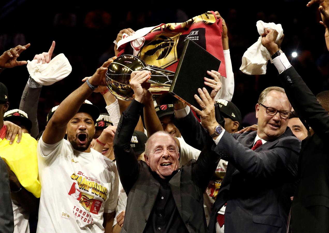 Norman Powell (i), jugador de los Toronto Raptors, y Larry Tanenbaum (c) y George Cope (d), miembros del grupo de propietarios de la franquicia, sostienen el trofeo.