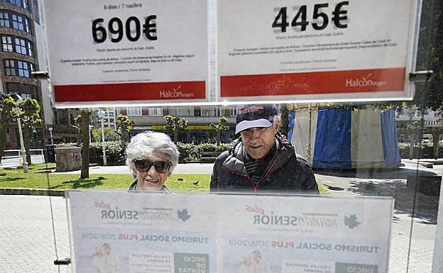 Una pareja de jubilados mira varias ofertas en el escaparate de una agencia de viajes. 