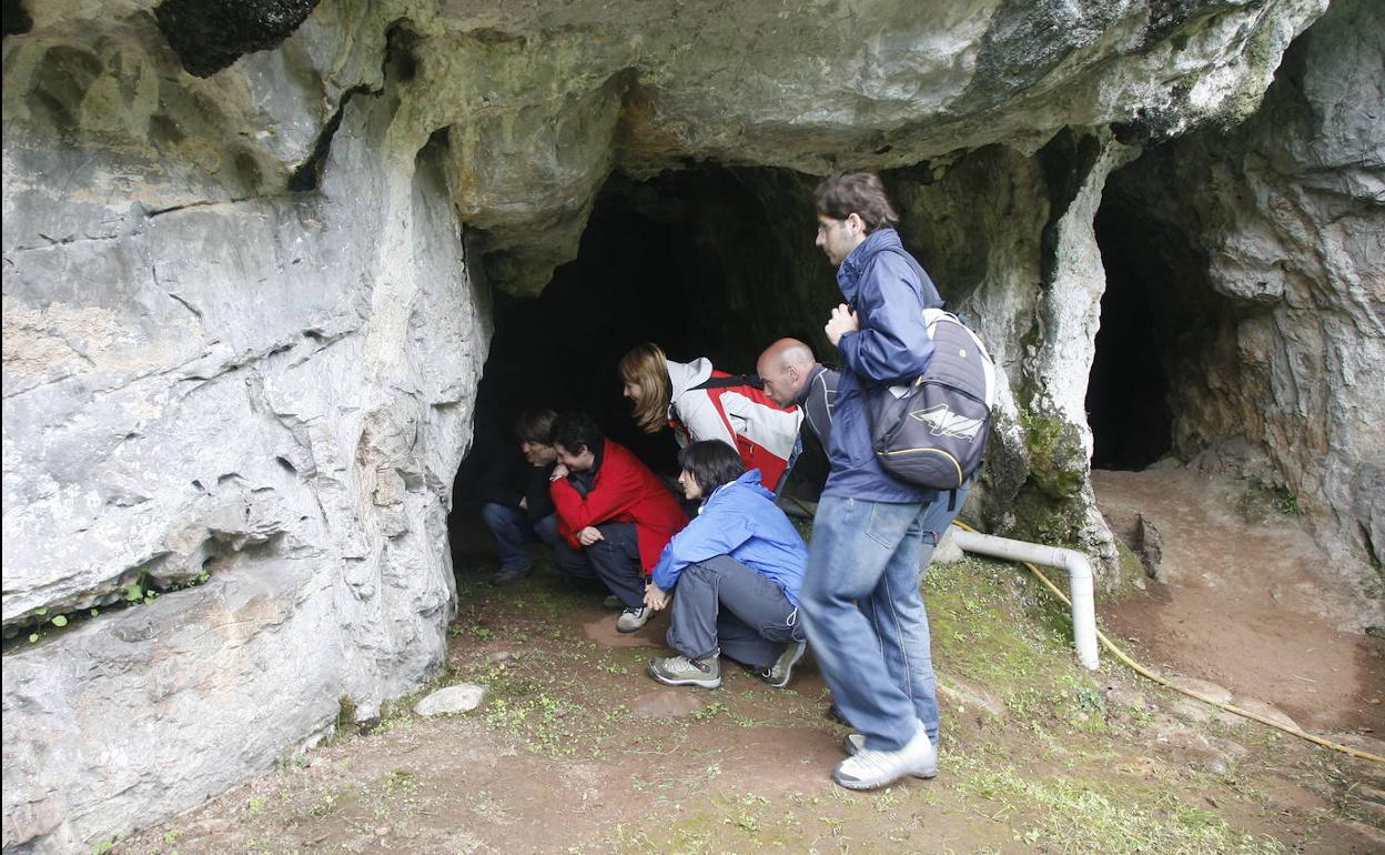 Varios visitantes observan los grabados del Paleolítico del abrigo de la cueva de La Lluera