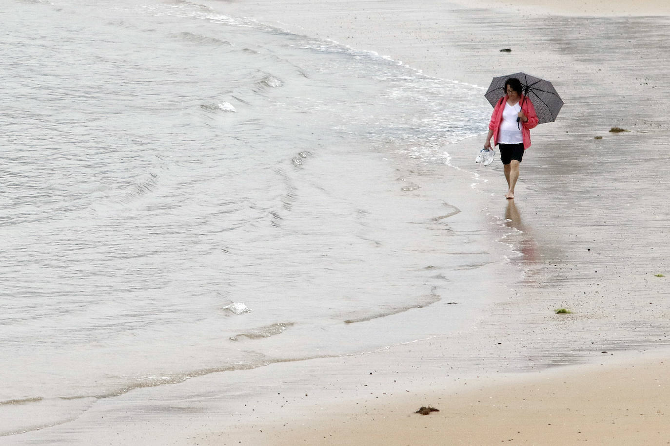 Una mujer camina por la playa de San Lorenzo con el paraguas. 