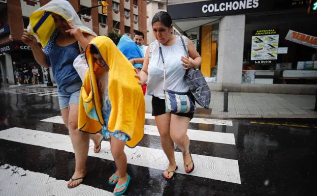 Un grupo de peatones se protege de la lluvia con toallas de playa.