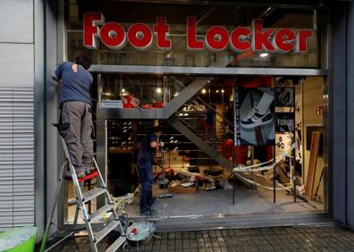 Imagen secundaria 1 - Arriba, una pintada en una calle de Barcelona. Abajo, operarios tratan de reparar los destrozos en una tienda. 