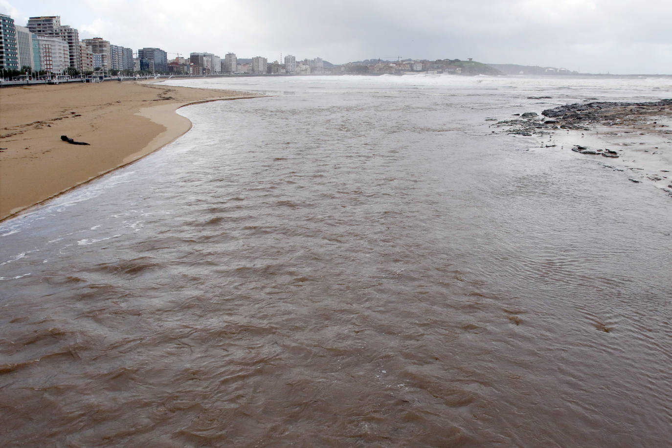 El temporal que azota Asturias ha ocasionado que la bahía de San Lorenzo apareciera este viernes con agua de color marrón, procedente del río Piles y del arrastre de las aguas de escorrentía, lo que se unió a una mar muy revuelta