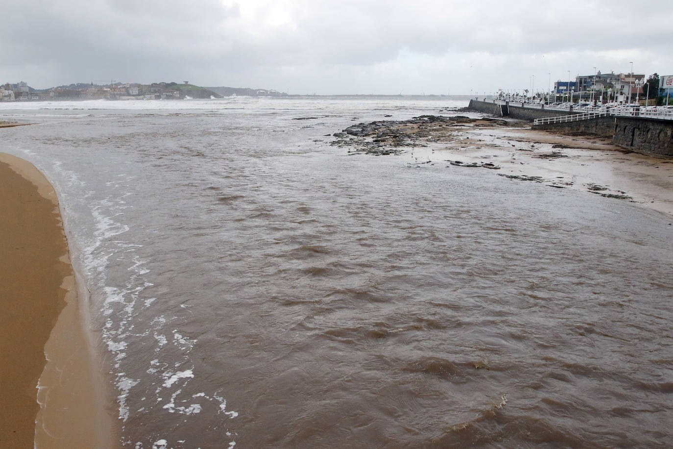 El temporal que azota Asturias ha ocasionado que la bahía de San Lorenzo apareciera este viernes con agua de color marrón, procedente del río Piles y del arrastre de las aguas de escorrentía, lo que se unió a una mar muy revuelta