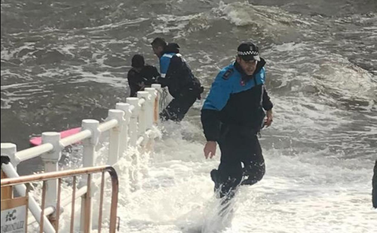 Dos policías ayudan al surfista a salir de la mar. 