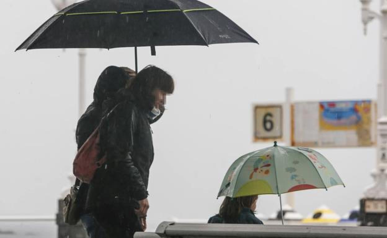 Dos personas caminan bajo la lluvia en Gijón.