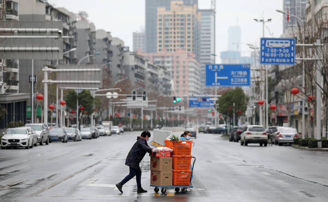 Una pareja arrastra un carro con verduras por una calle desierta de Wuhan, en China.