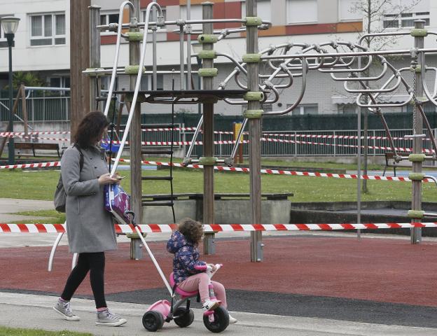 Una mujer pasa con su hija frente a un área de juegos infantiles clausurada en Nuevo Roces. 