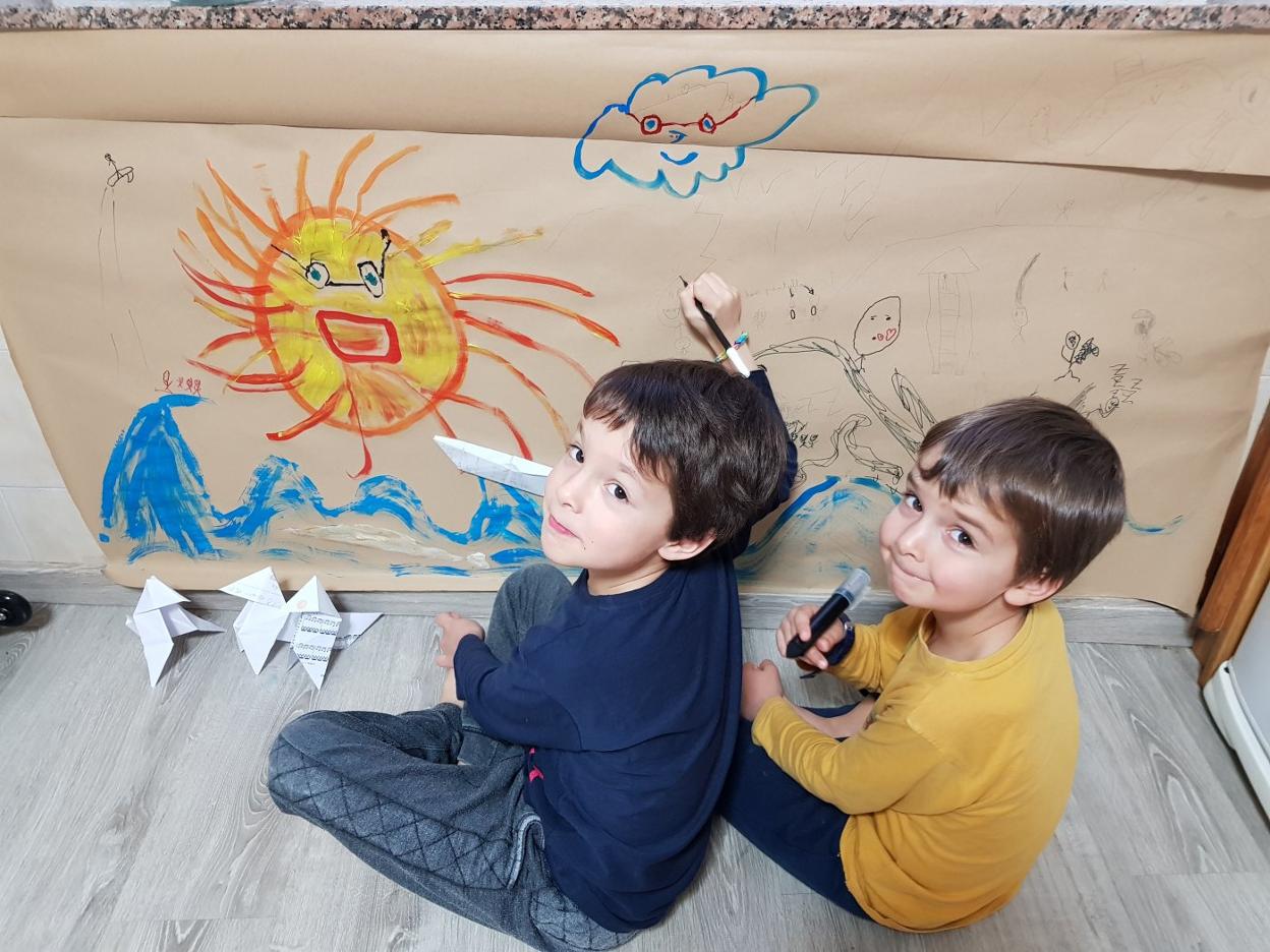 Jacobo y Beltrán, de 7 y 6 años, pintan una playa en la pared de su casa. Junto a ellos, las piezas de origami hechas con su madre. 