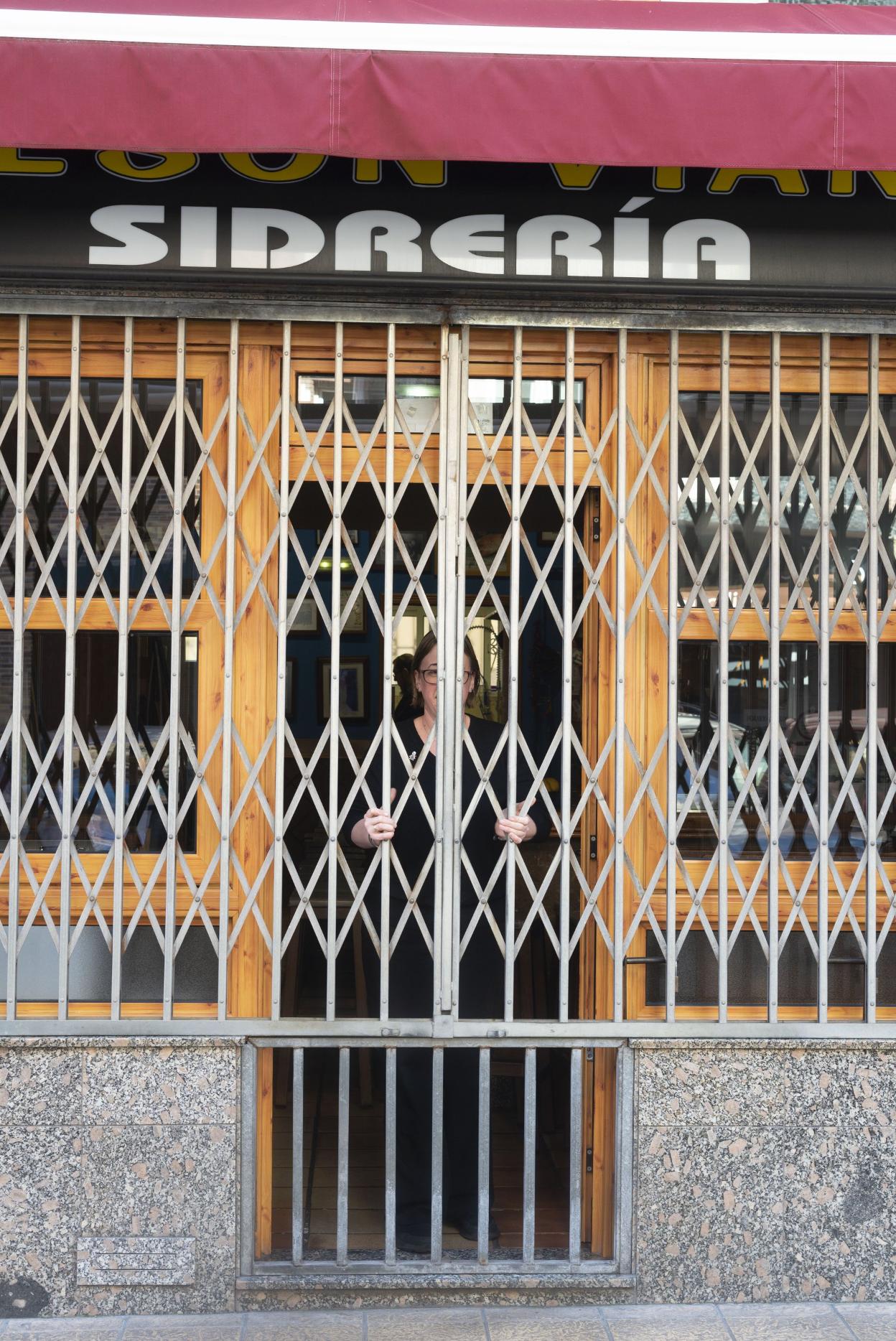 Una mujer cierra la verja de una sidrería. 