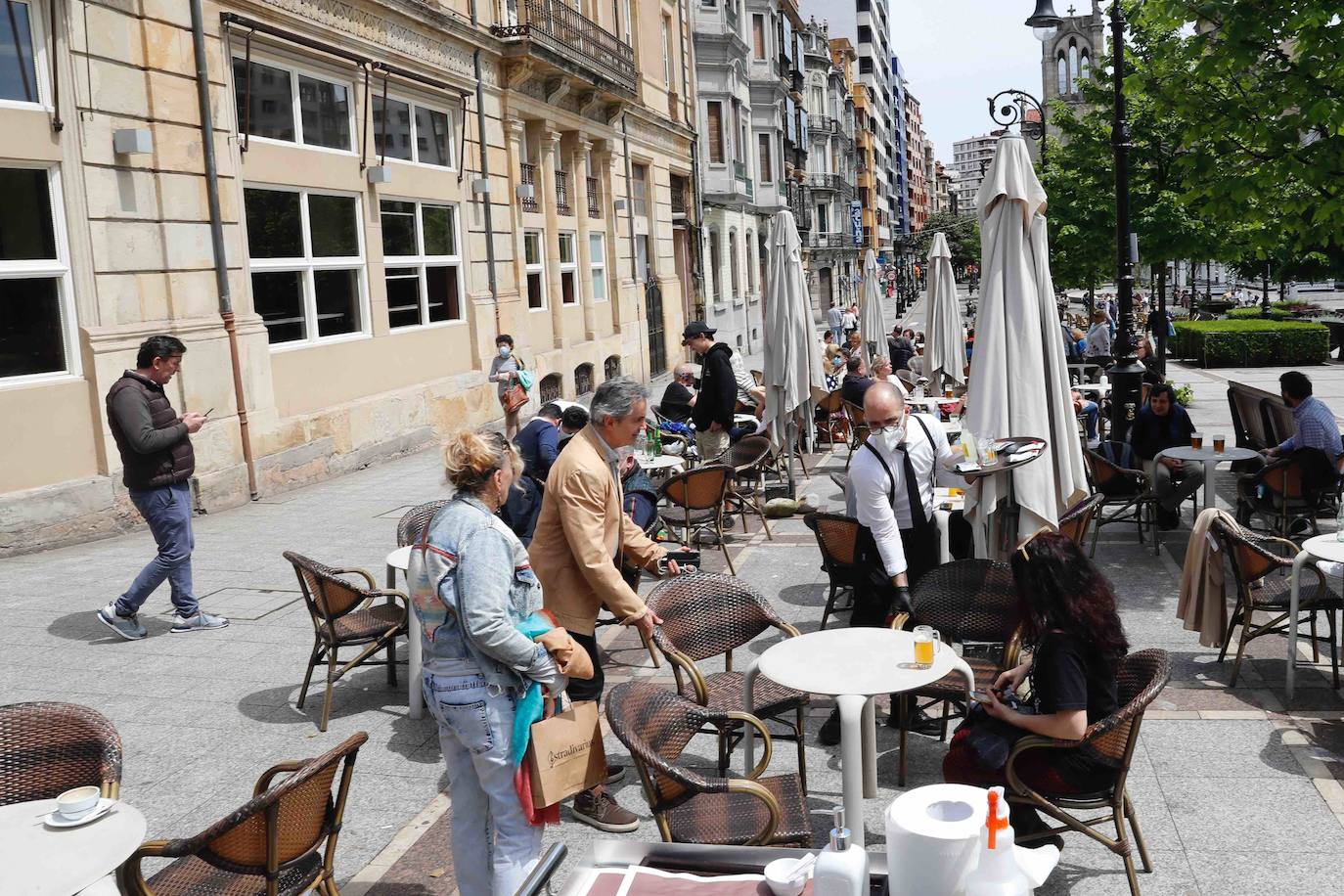Tras ocho semanas con las verjas bajadas y las sillas y mesas apiladas, los establecimientos hosteleros de Gijón han vuelto a colocar sus terrazas. Eso sí, bajo estrictas medidas de higiene y aforo para prevenir el contagio de coronavirus. 
