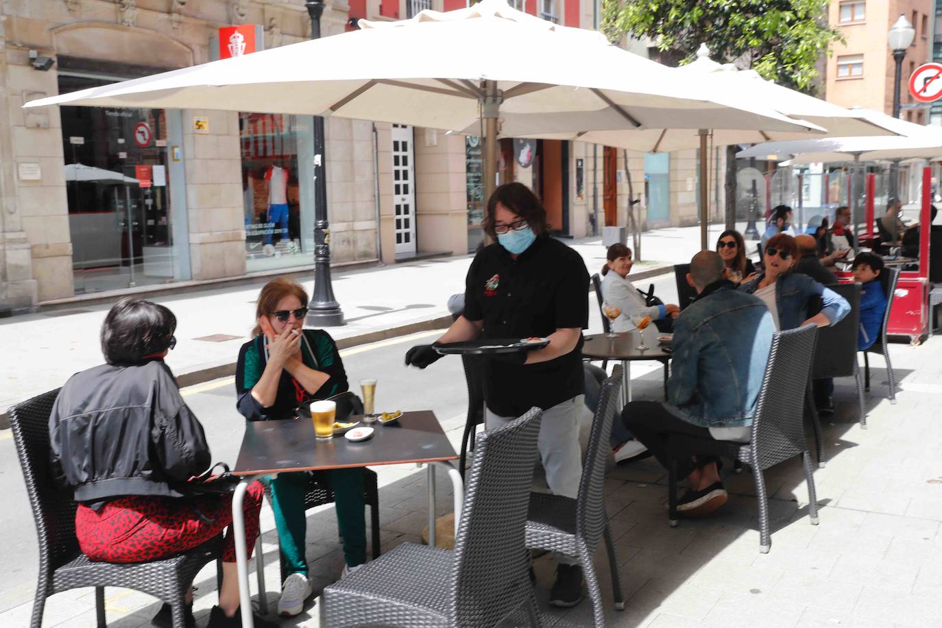 Tras ocho semanas con las verjas bajadas y las sillas y mesas apiladas, los establecimientos hosteleros de Gijón han vuelto a colocar sus terrazas. Eso sí, bajo estrictas medidas de higiene y aforo para prevenir el contagio de coronavirus. 