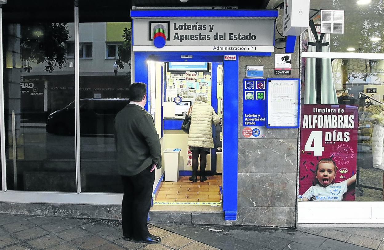 Un cliente espera su turno a las puertas de una administración de lotería en Gijón. 