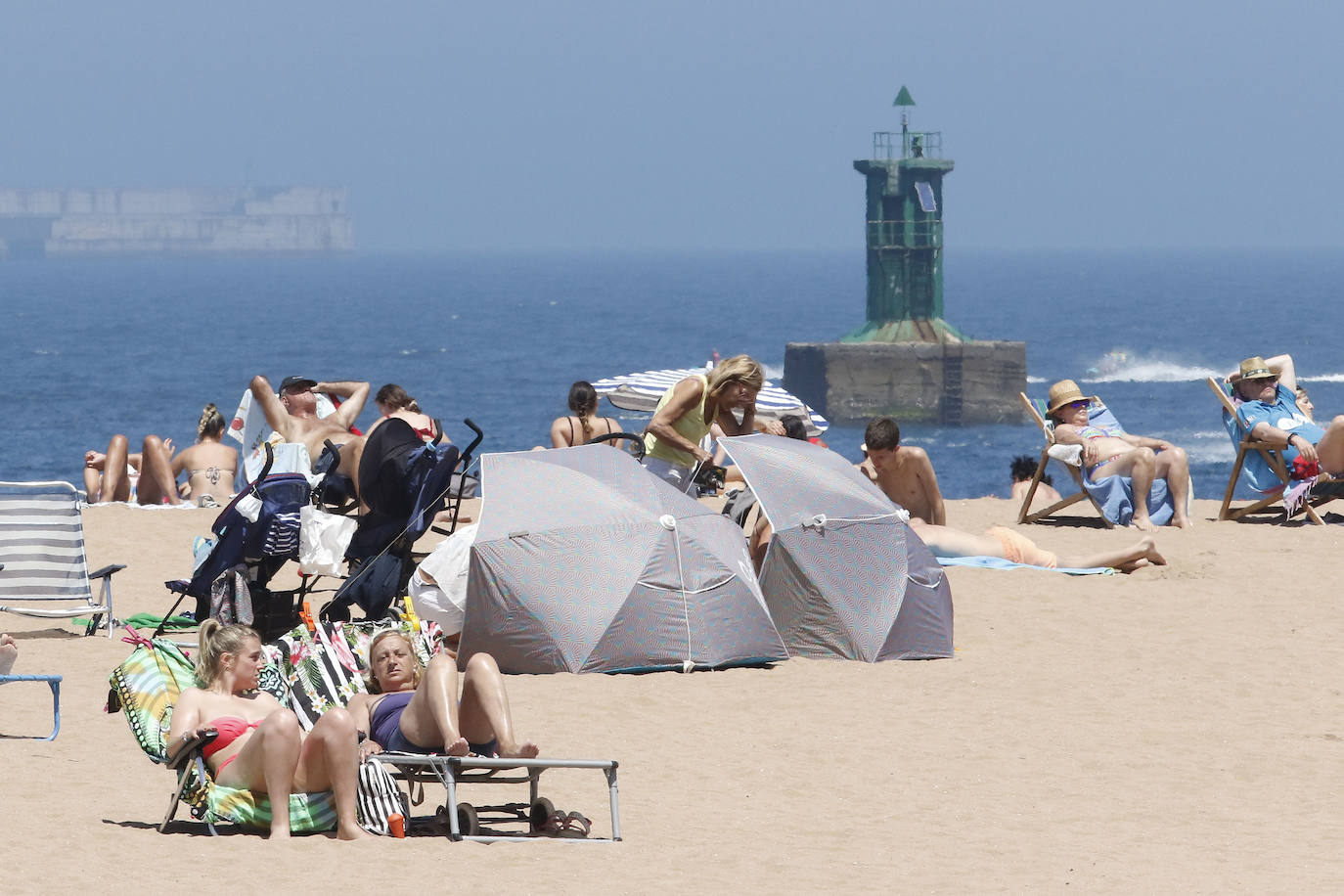 Los arenales gijoneses han vuelto este martes a llenarse de gente que ha querido pasar una nueva jornada de intenso calor tumbado en la arena o refrescándose en el agua.