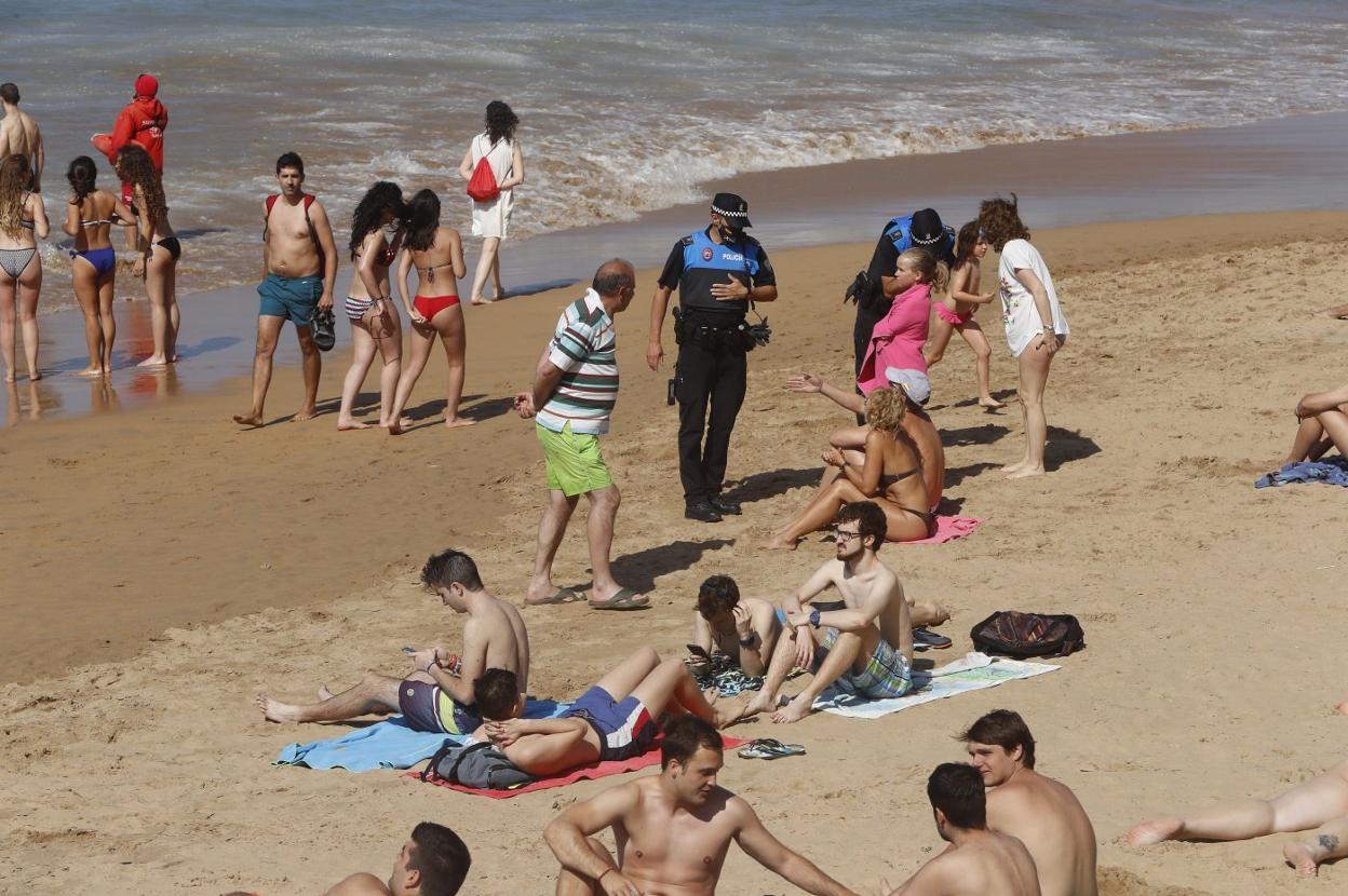 Dos agentes, en la playa de San Lorenzo, avisan a varias personas de que tienen que cambiar de sitio. 