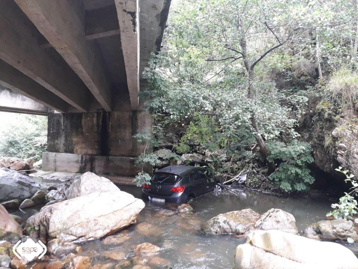 El turismo accidentado, en el río, tras caer desde una altura de ocho metros en Las Ventas (Proaza). 
