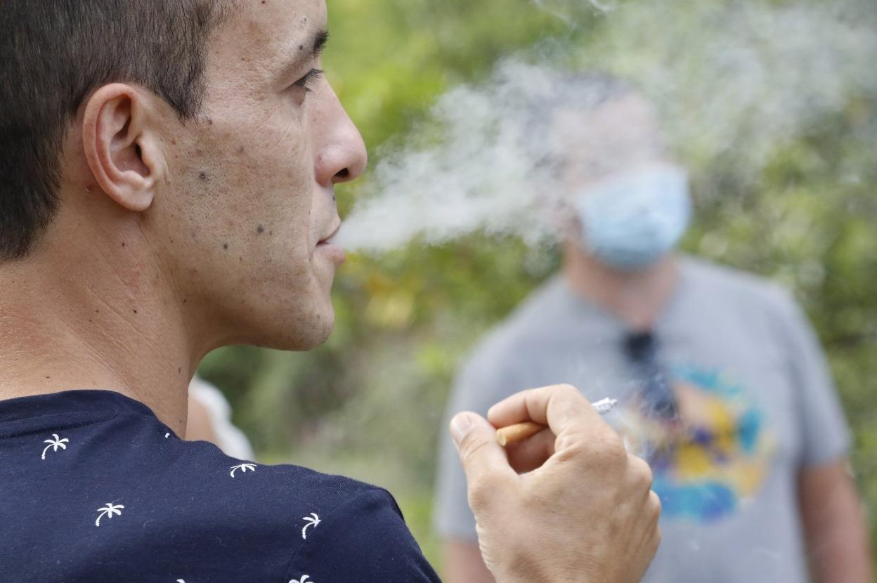 Un joven fuma un cigarrillo en la vía pública en presencia de otras personas. 