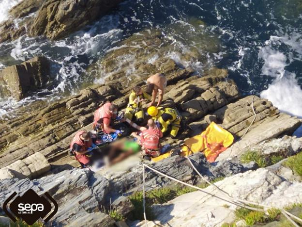 Efectivos del Grupo de Rescate del SEPA y bomberos del parque de Barres inmovilizan al varón herido en El Franco para su evacuación. 