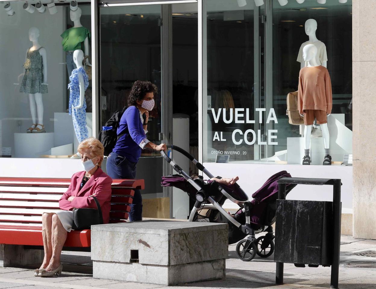 Una mujer pasea con el carrito de un niño junto a una tienda con la campaña de la 'vuelta al cole' en Oviedo. 