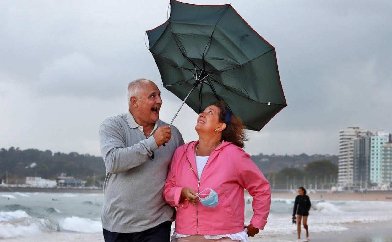 Una pareja pasea en un día de lluvia por la playa de San Lorenzo de Gijón. 