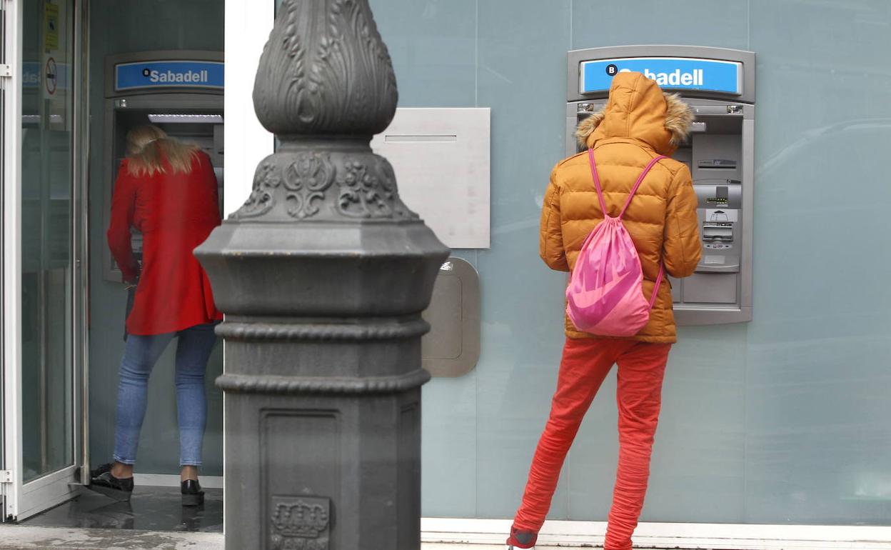 Dos personas sacan dinero de los cajeros de una sucursal bancaria.