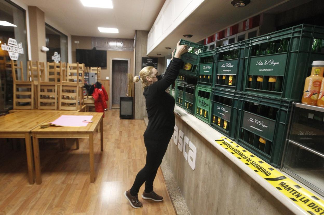 Una mujer apila cajas de sidra para preparar el cierre de su sidrería. 