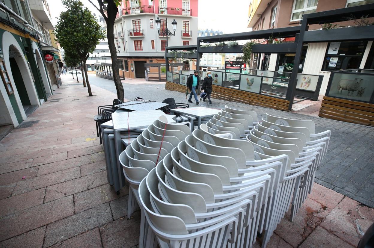 Una pareja de transeúntes pasean por una desierta calle Gascona, con las mesas y las sillas de los bares apiladas. 