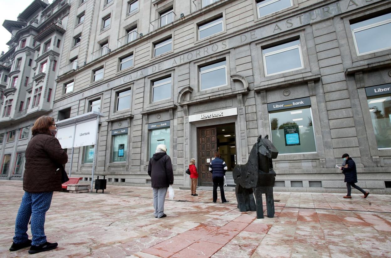 Unos clientes guardan cola ante los cajeros de Liberbank en su sede central, en Oviedo. 