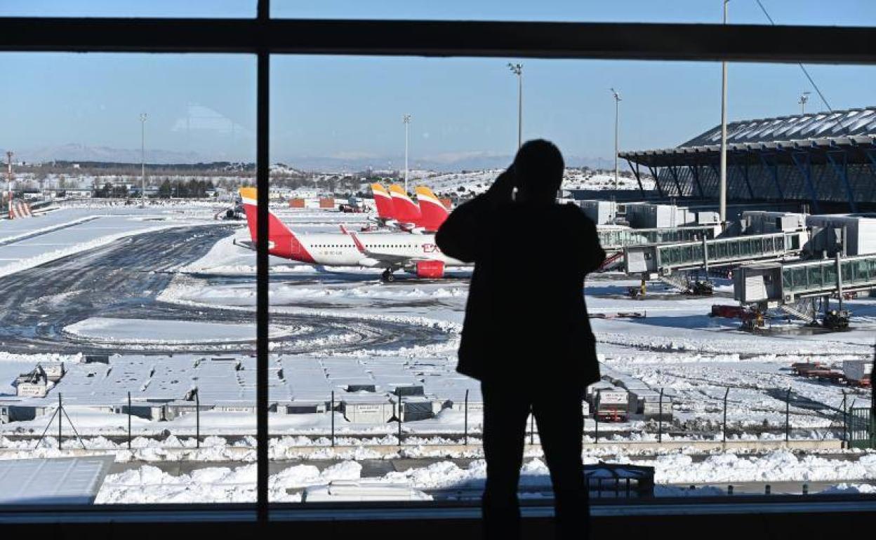 Un viajero toma observa las pistas en la Terminal 4 del aeropuerto Adolfo Suárez Madrid-Barajas cubiertas parcialmente de nieve este lunes 
