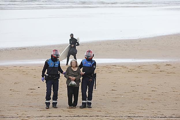 Dos policías, con la mujer rescatada. El surfista que la rescató, al fondo de la imagen. 
