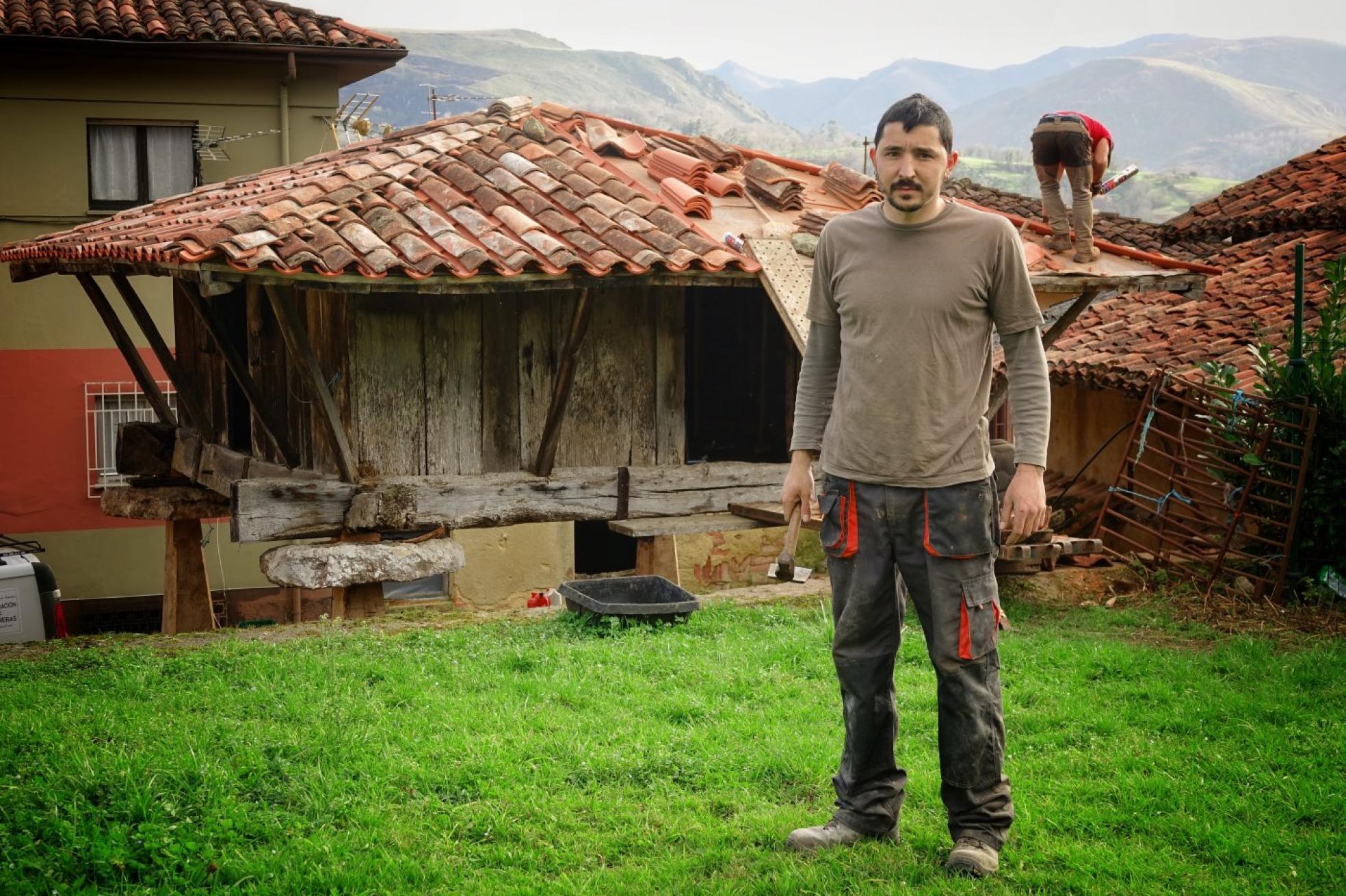 San Román (Piloña).Adrián Castañedo, ante el hórreo en el que está trabajando estos días. 
