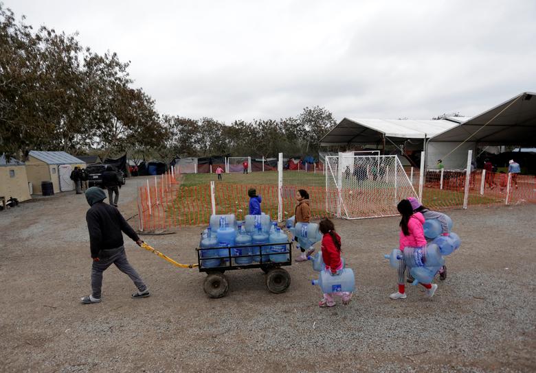 Migrantes que viajaron al norte de México en busca de asilo en los Estados Unidos, son vistos cargando jarras de agua vacías en un campamento de migrantes en Matamoros.