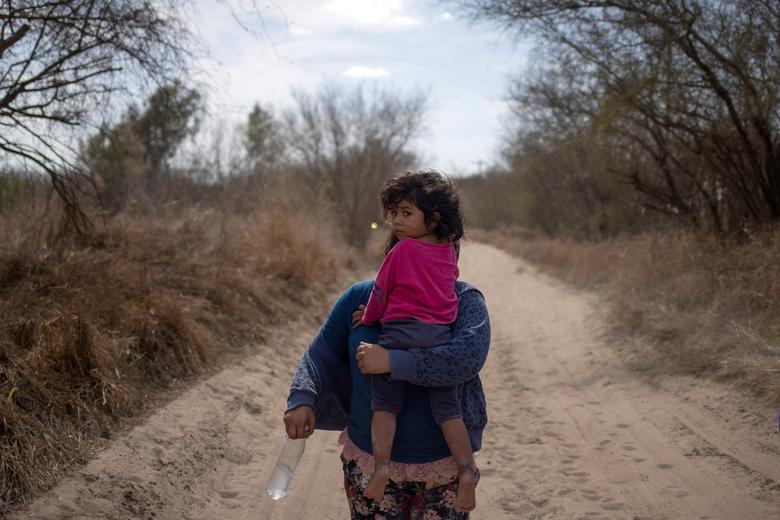 María, de 4 años, de El Salvador, es sostenida por su madre Loudi mientras caminan por un camino de tierra después de cruzar el río Grande hacia los Estados Unidos desde México en Penitas, Texas.