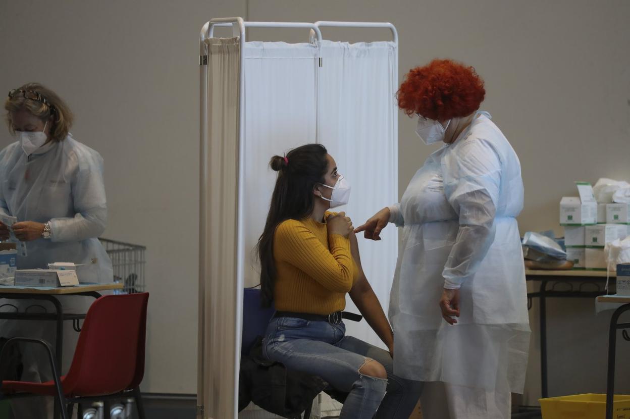 Una joven recibe indicaciones sobre las posibles reacciones de la vacuna tras recibir el pinchazo. 