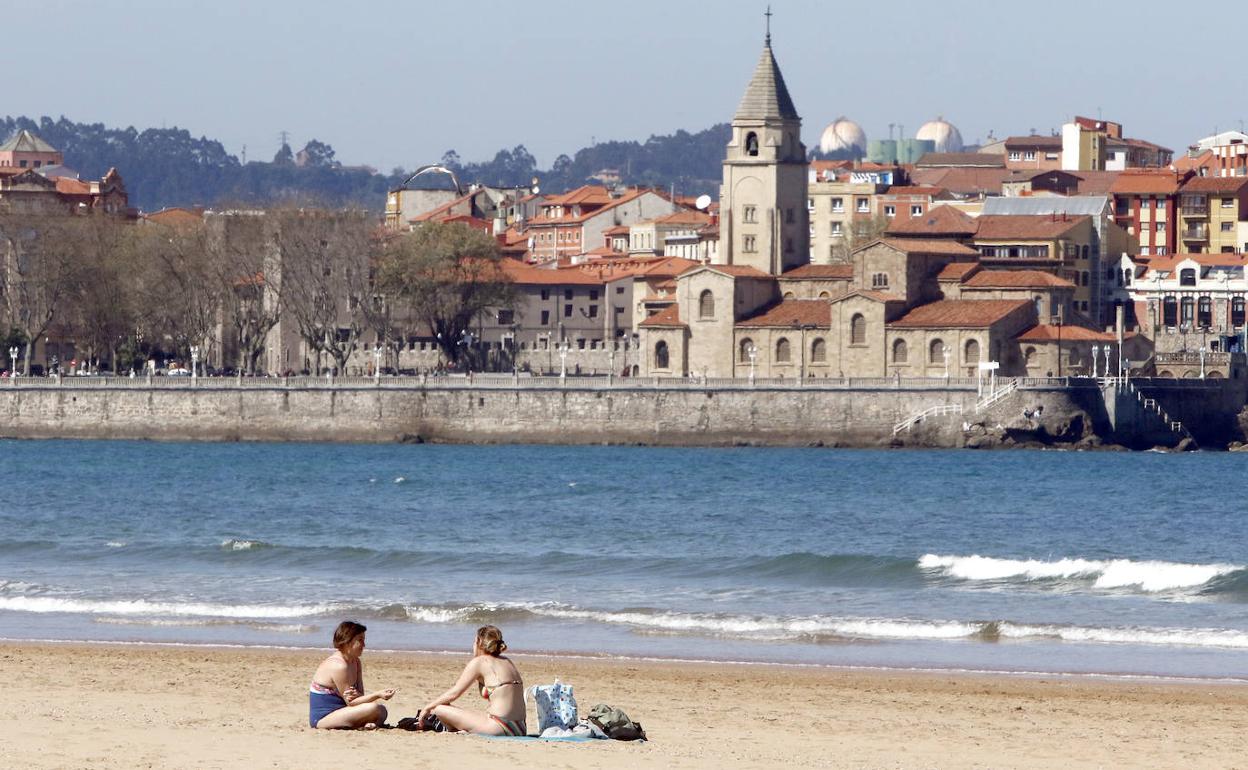 Dos personas toman el sol en la playa de San Lorenzo de Gijón 