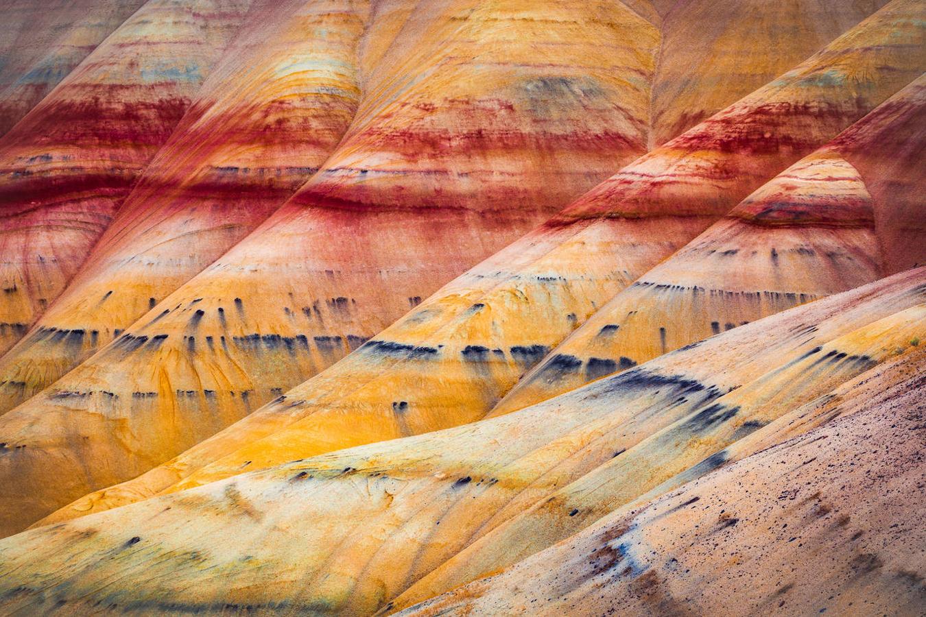 Las colinas pintadas de Oregón: Estas colinas, llamadas así por las capas de colores y estrías en bandas que pueden verse en sus colinas y que son resultado de las diferentes eras geológicas, son una de las tres partes que conforman el Monumento Nacional John Day Fossil Beds en el condado de Wheeler, en Oregon (EE.UU). Unos colores que varían en función de la hora del día y de las estaciones del año, aunque el mejor momenro para disfrutar de su manto de color aseguran que es después de una tormenta, cuando los colores rojizos, ambar, dorados, amarillos, negros y grises se intensifican.