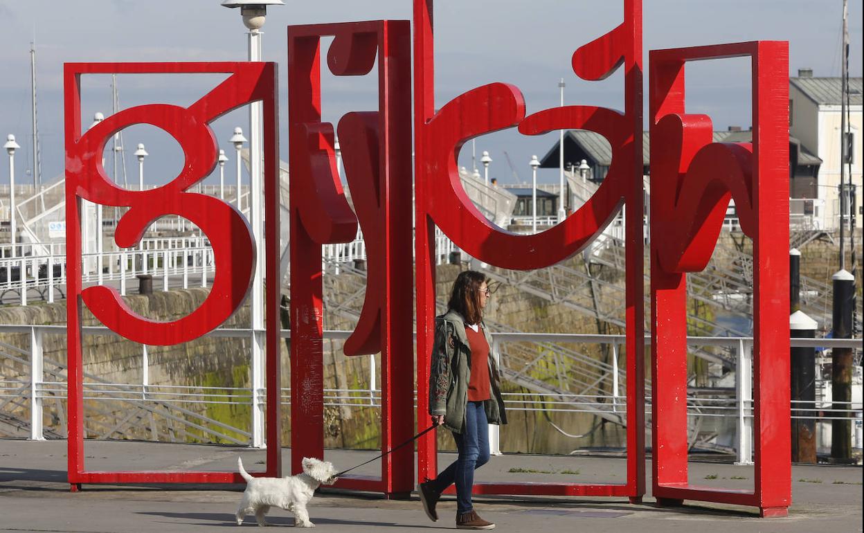 Una mujer pasea al perro delante de las letronas de Gijón