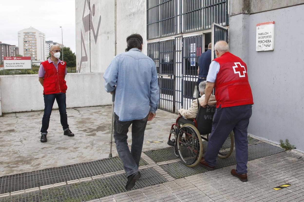 Un voluntario de Cruz Roja ayuda a una persona mayor a acceder a la zona de vacunación en Perchera. 