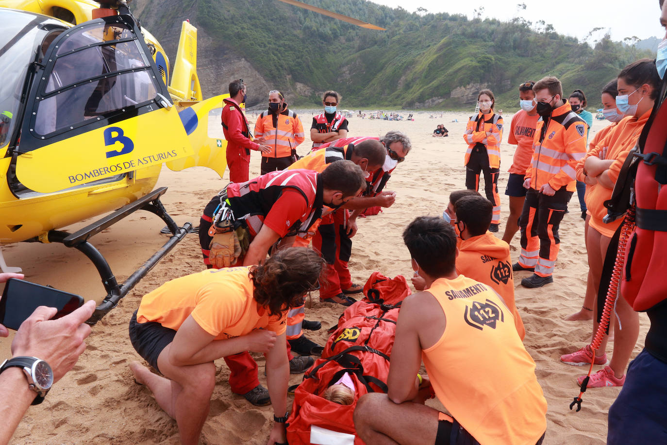 El helicóptero del Servicio de Emergencias del Principado realizó esta mañana un simulacro en la playa de Rodiles. La actuación, que contaba con la participación de más de veinte profesionales, despertó la curiosidad entre los bañistas. El objetivo de este simulacro es enseñar a los socorristas cómo actuar en caso de emergencia durante este verano. El equipo rescatador explicó cuál es la mejor zona para el aterrizaje y cómo deben prepararse.